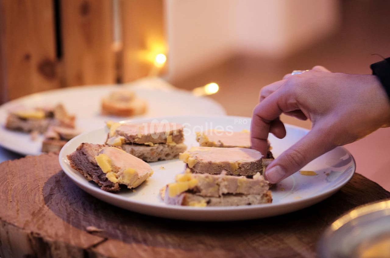 Main prenant une tranche de pain avec du foie gras sur une assiette, dans un contexte de repas convivial.