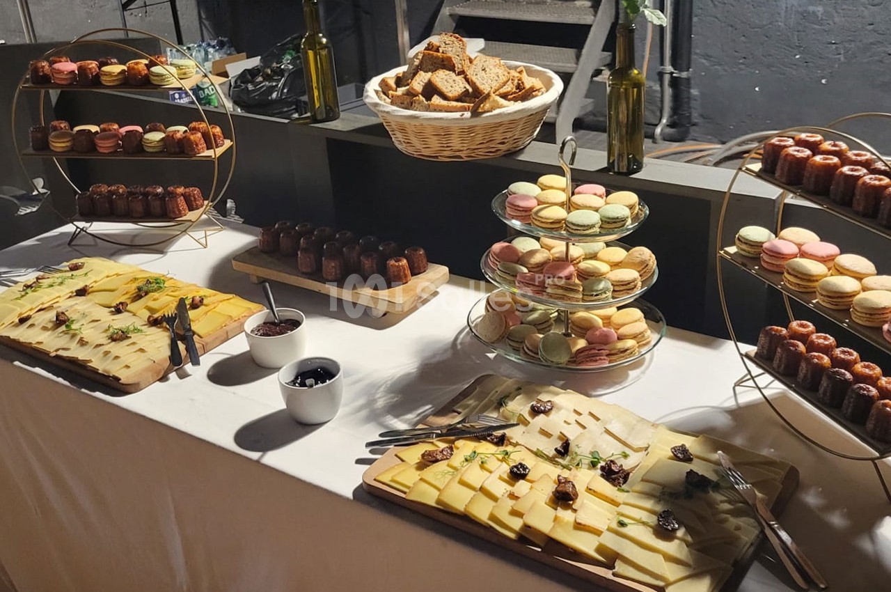 Buffet avec plateaux de fromages, macarons, cannelés, pain et olives, présenté sur une table blanche.
