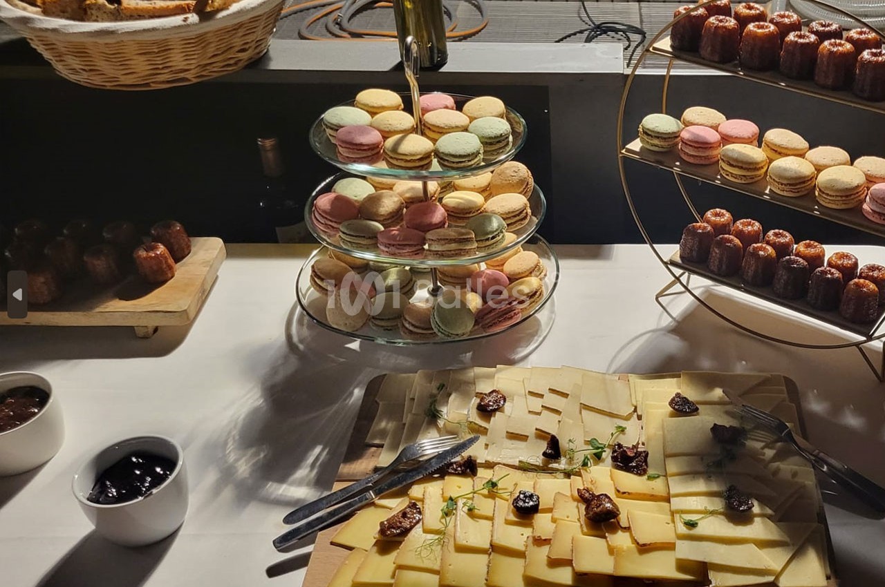 Plateau de fromages avec confitures, macarons colorés sur présentoirs et cannelés disposés sur une table.