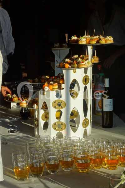 Plateau de bouchées apéritives sur un présentoir décoratif, entouré de verres de boisson et d'une bouteille de vin.