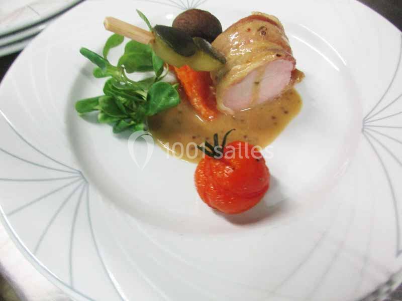 Roulé de volaille avec sauce, accompagné de légumes grillés, salade verte et tomate cerise sur une assiette blanche.