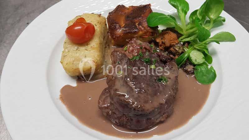 Assiette composée d'un filet de viande en sauce, gratin, légumes, champignons et mâche, présentée sur une table.