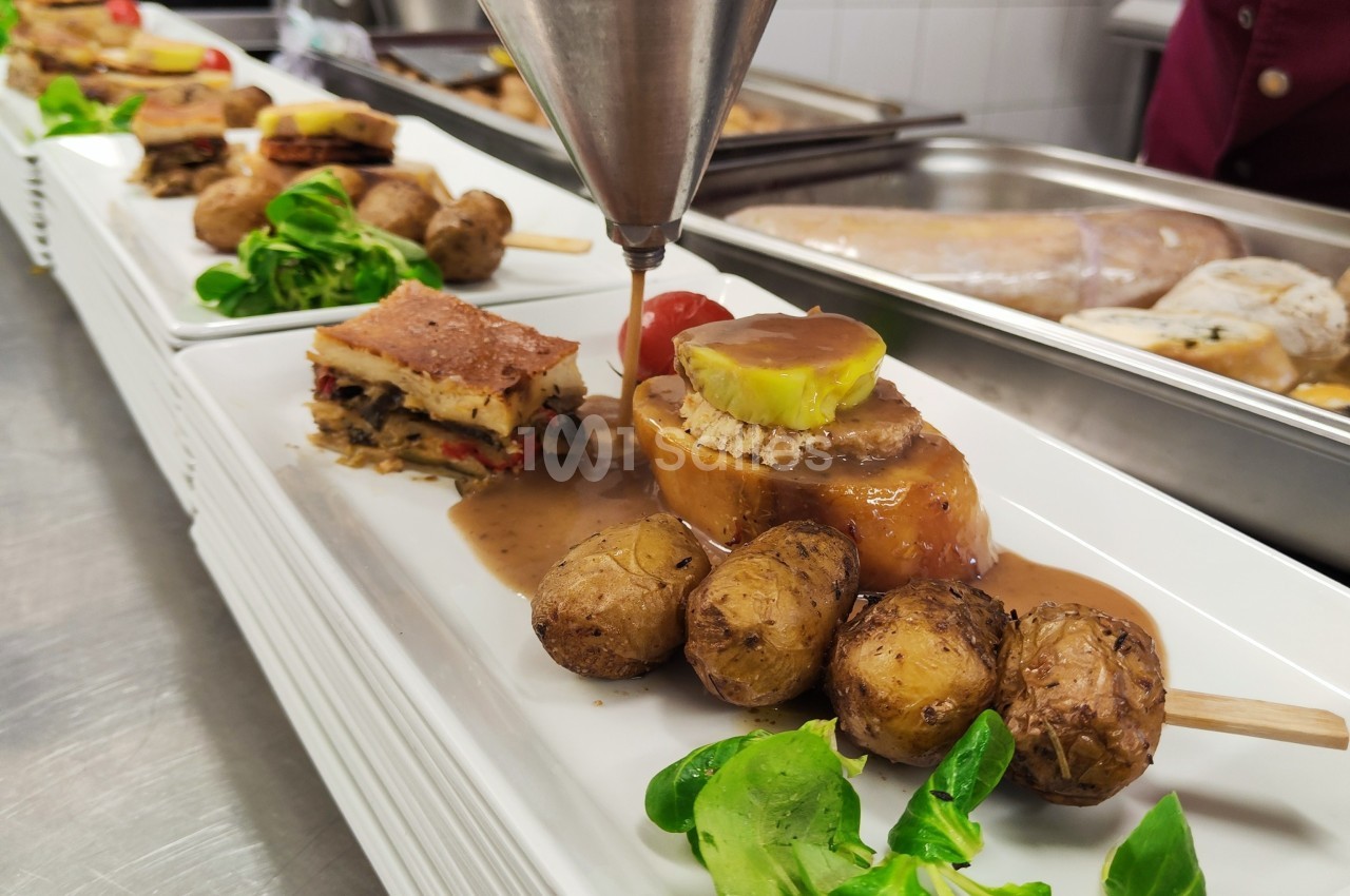 Assiette gastronomique avec viande en sauce, pommes de terre rôties, légumes et garniture, en cours de dressage.