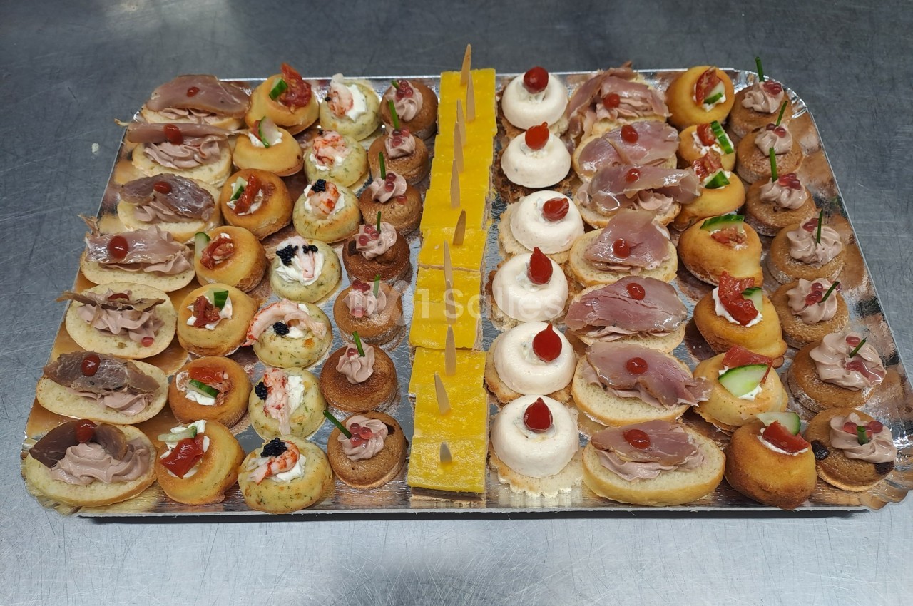 Plateau de canapés variés comprenant des bouchées salées et sucrées, disposées sur une table en inox.