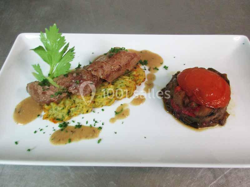 Assiette composée de viande, galette de légumes, sauce, et accompagnement de légumes grillés avec tomate.