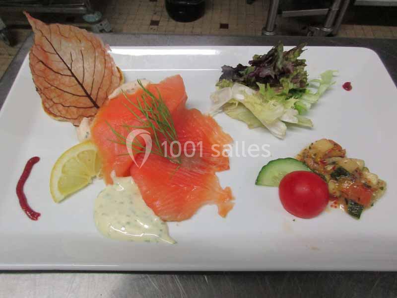 Assiette de saumon fumé avec crème, citron, salade, légumes marinés, tomate cerise et décoration de feuille.