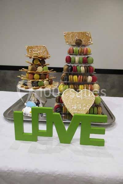 Deux pyramides de macarons colorés sur un plateau, décorées de biscuits et entourées du mot ’LOVE’ en lettres vertes.
