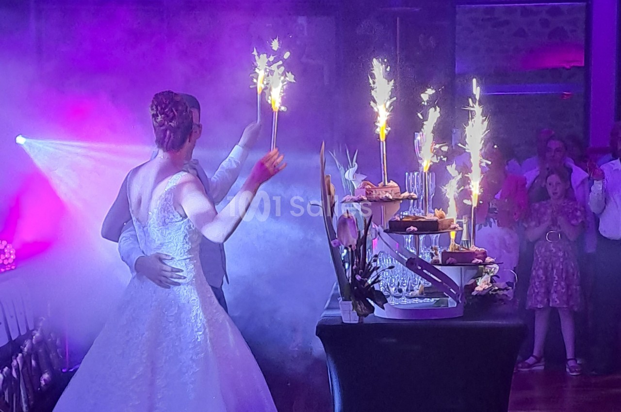 Un couple de mariés danse près d'une table de desserts illuminée par des cierges magiques, entouré d'invités.