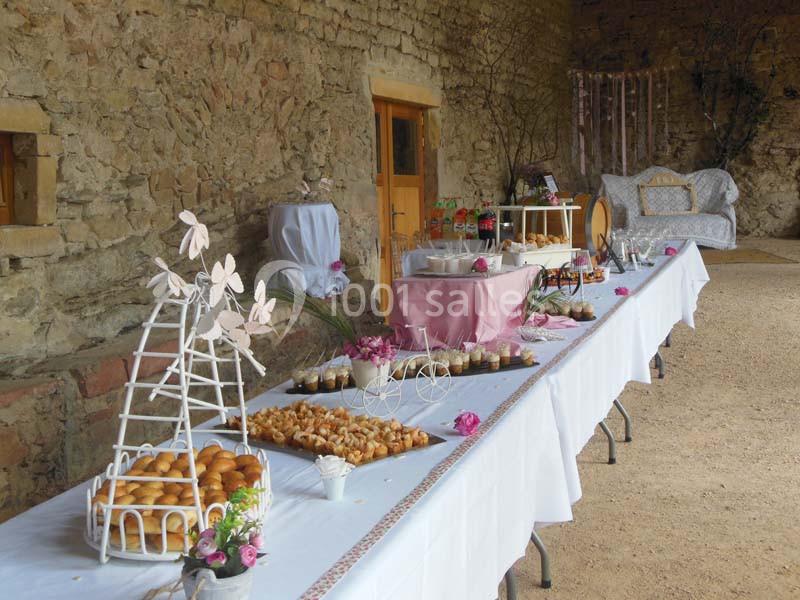 Table de buffet décorée avec des fleurs roses, disposée dans un espace en pierre avec des desserts et des amuse-bouches.