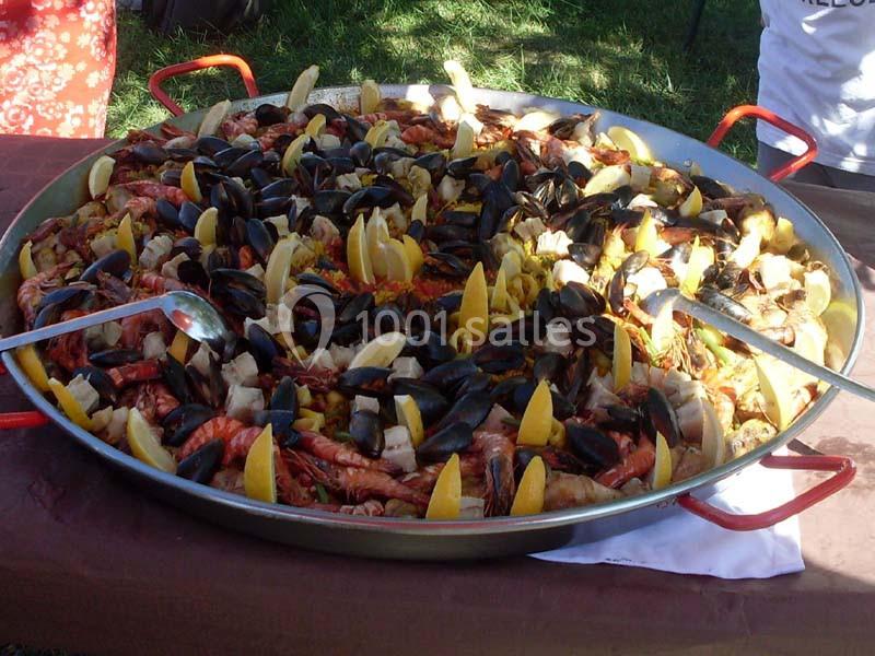 Grande paella garnie de fruits de mer, moules, crevettes et quartiers de citron, servie dans un plat rond en extérieur.