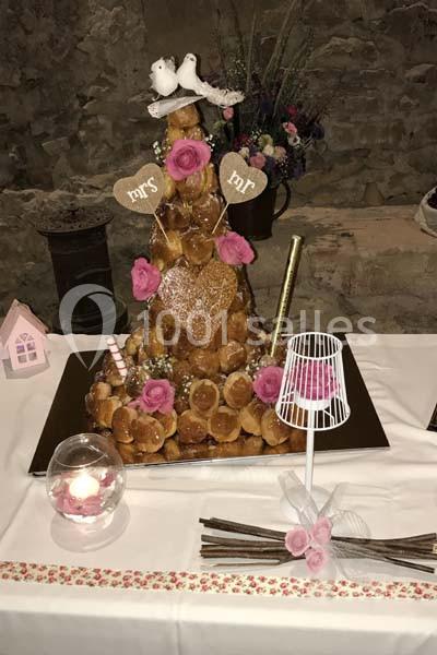 Pièce montée en choux décorée de roses, de cœurs en bois et de figurines d'oiseaux, posée sur une table blanche.