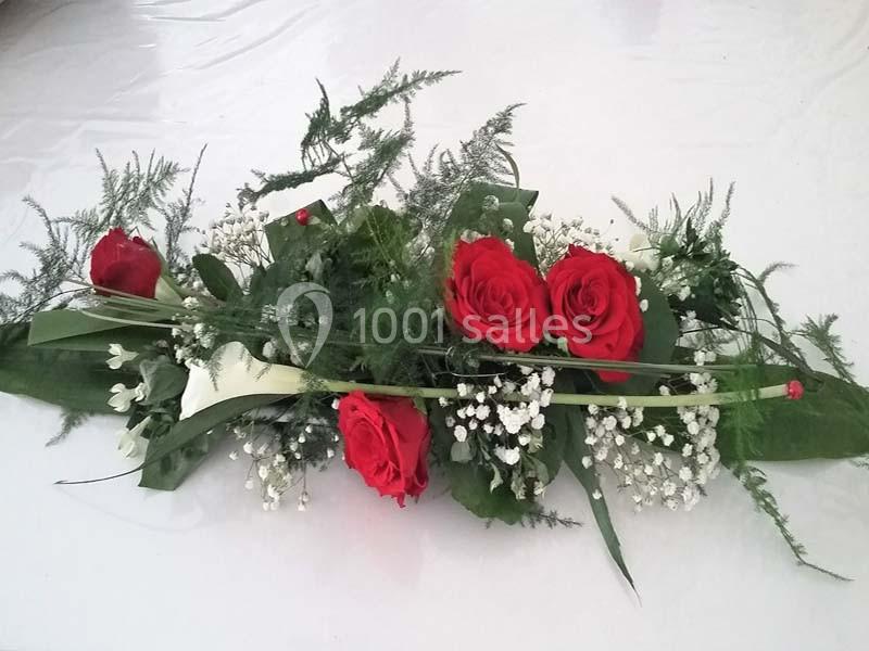 Arrangement floral avec des roses rouges, du gypsophile blanc et des feuillages verts sur une surface blanche.