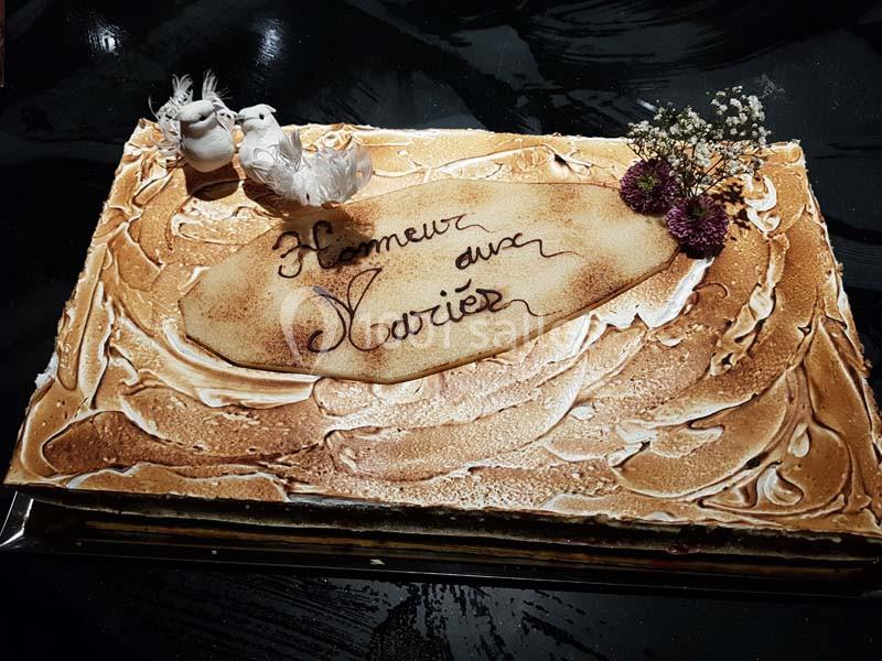 Gâteau rectangulaire décoré de meringue dorée, fleurs séchées et figurines d'oiseaux, avec l'inscription ’Honneur aux Mariés…