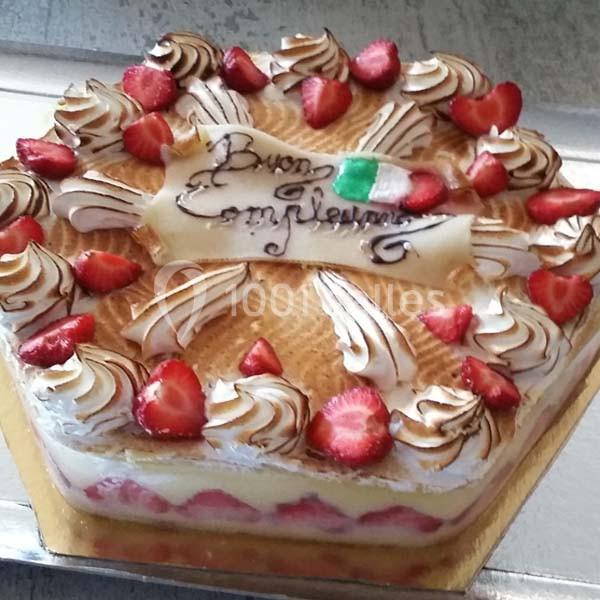 Gâteau décoré de fraises, meringue et inscription en italien sur un dessus en crème dorée.