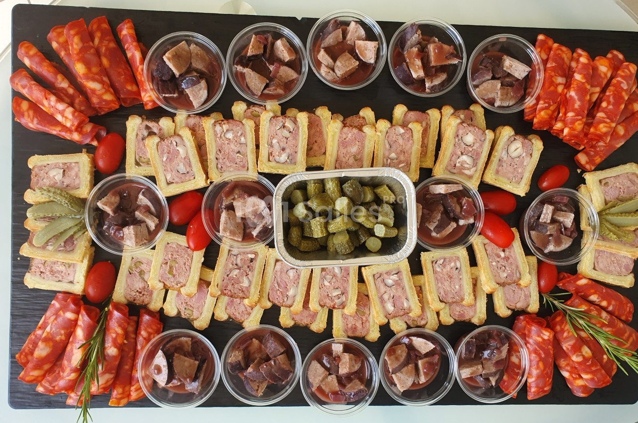 Plateau de charcuterie avec pâtés, saucissons, cornichons, tomates cerises et ramequins de terrines disposés symétriquement.