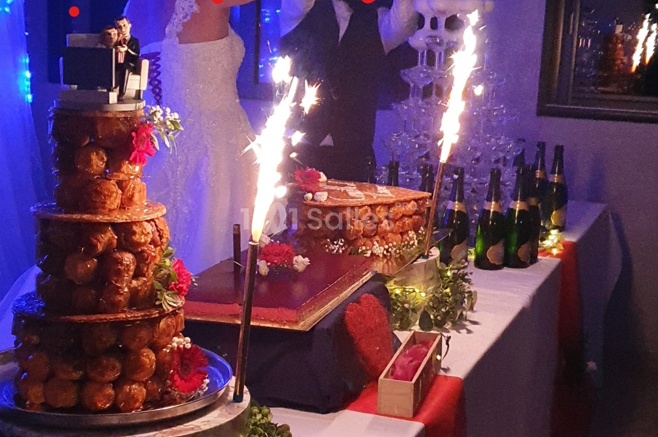 Pièce montée en choux et gâteau entourés de décorations festives, avec des bouteilles de champagne en arrière-plan.