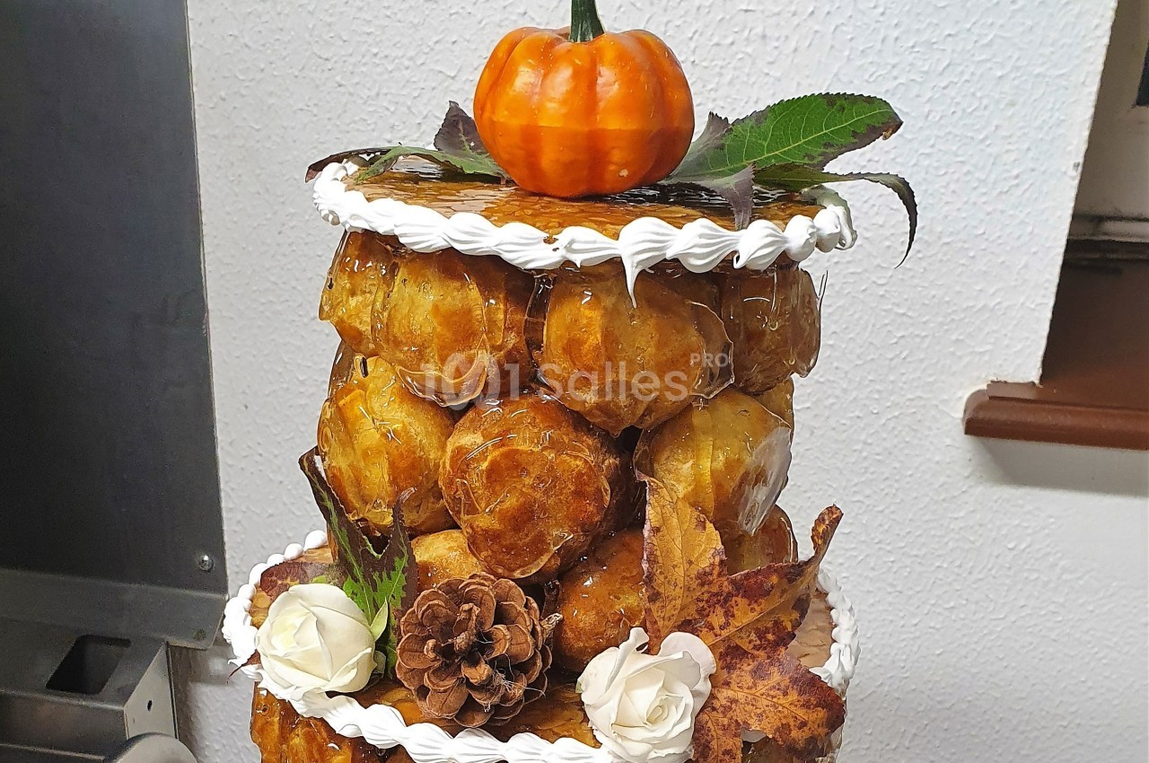 Pièce montée en choux caramélisés décorée de feuilles, fleurs, pomme de pin et une petite citrouille au sommet.