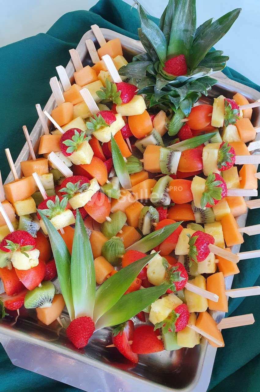 Brochettes de fruits frais variés, disposées sur un plateau avec des décorations d'ananas et de fraises.