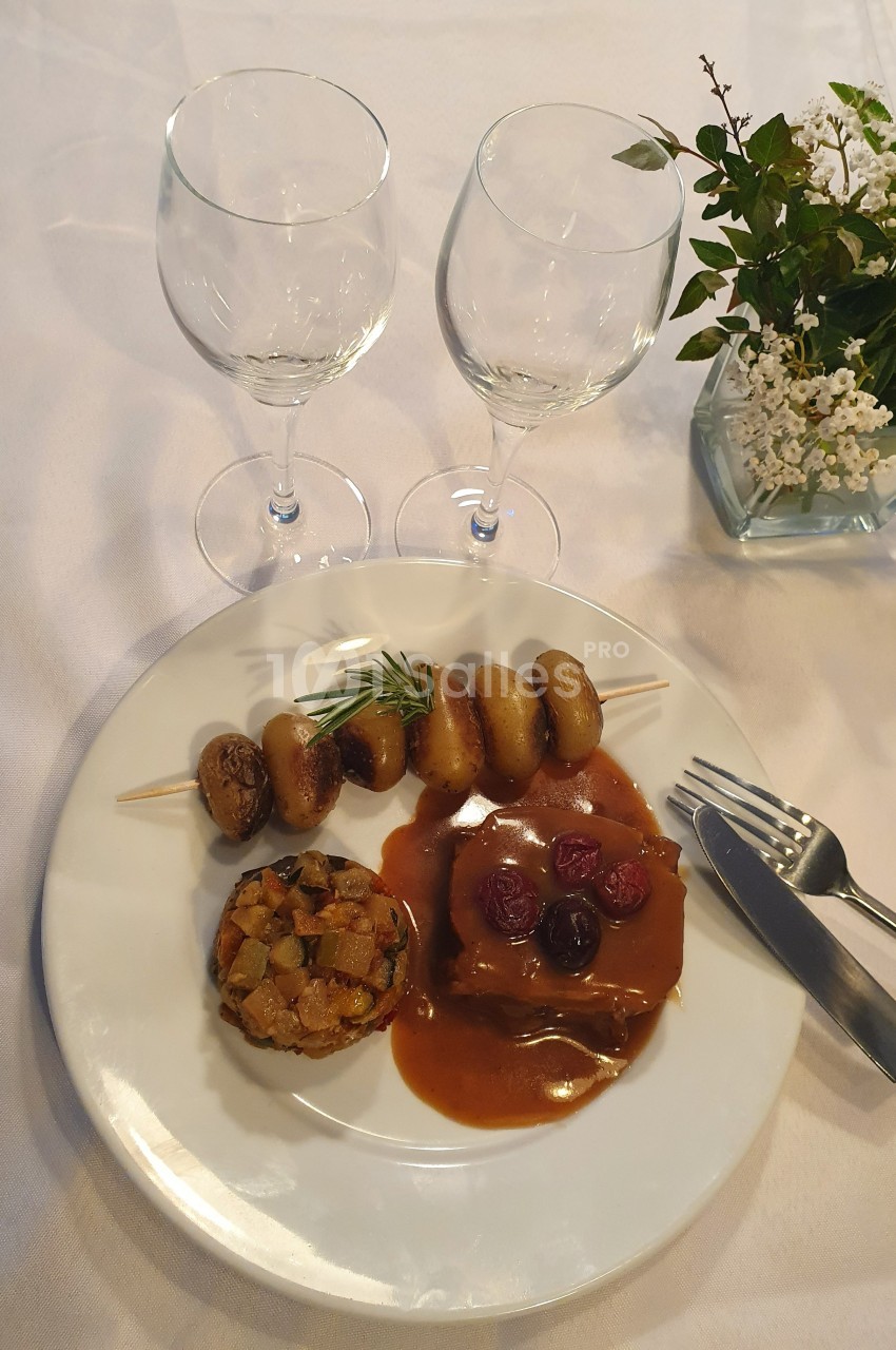 Assiette gastronomique avec viande en sauce, brochette de pommes de terre, légumes sautés et décoration florale en arrière…