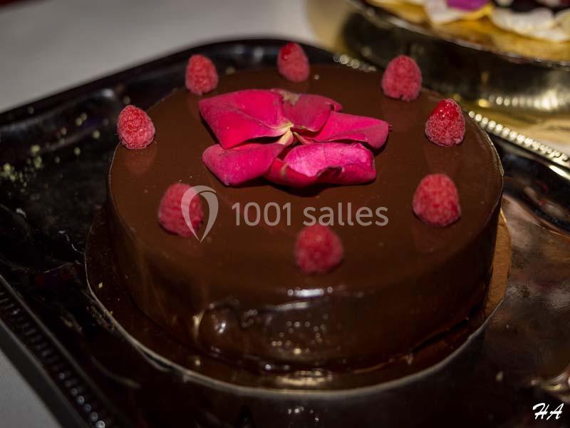 Gâteau au chocolat décoré de framboises et d'une fleur rose, présenté sur un plateau sombre.