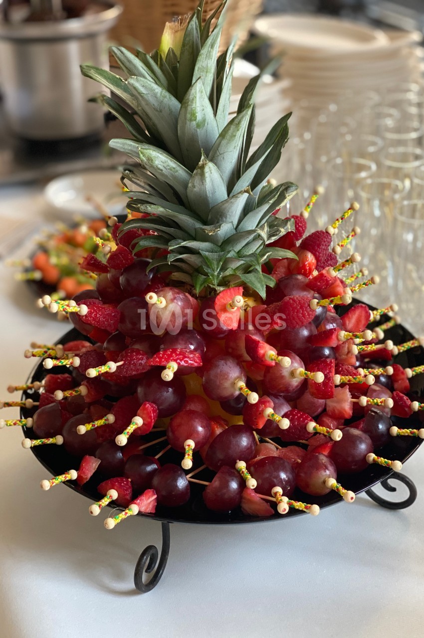 Brochettes de fruits variés, principalement raisins et fraises, disposées autour d'un ananas sur un plateau.