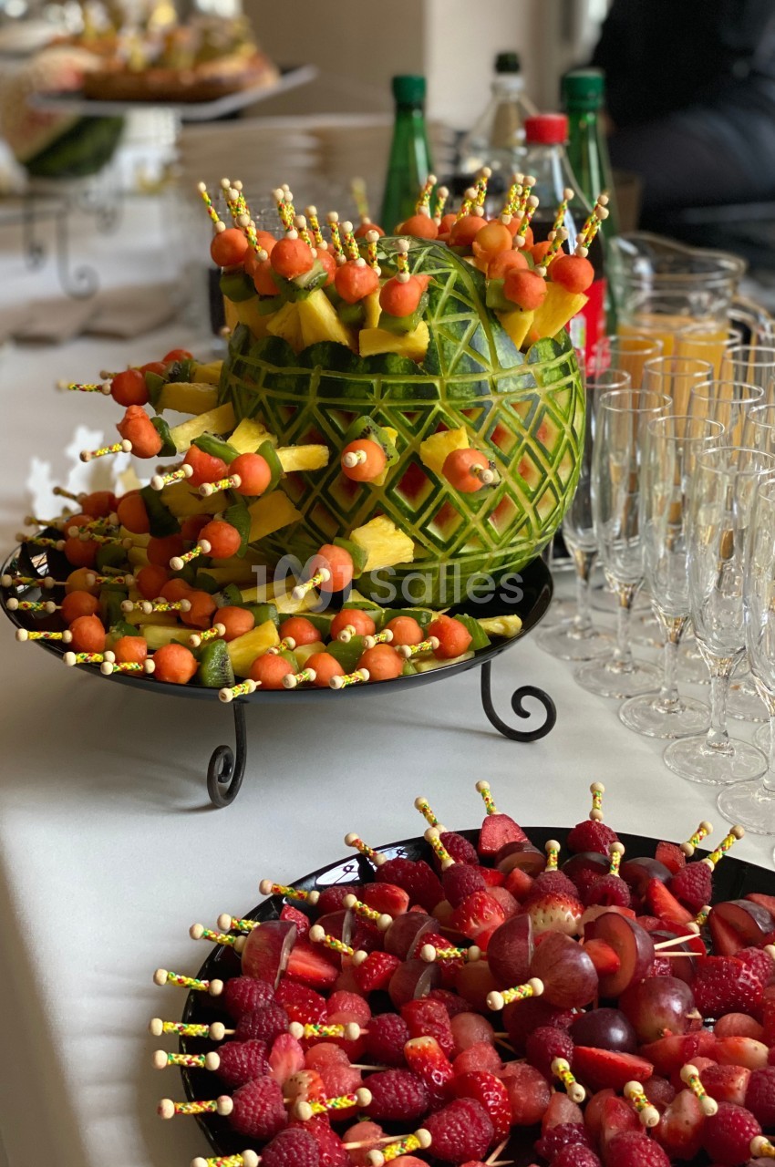 Plateau de fruits décoratif avec brochettes de melon, ananas et fraises, disposé sur une table de réception.