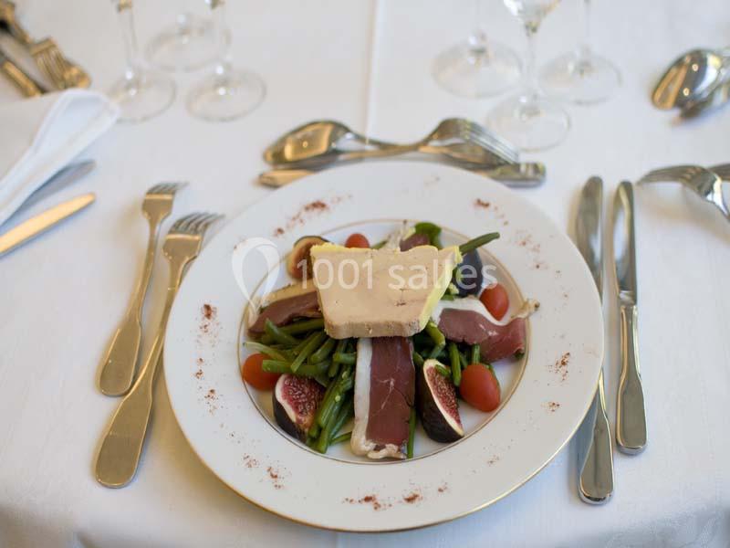 Assiette dressée avec haricots verts, tomates cerises, figues, magret de canard et tranche de fromage sur une table élégante.