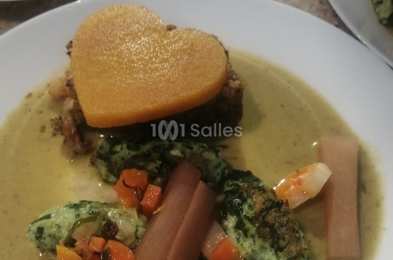 Assiette contenant un plat composé de légumes, quenelles vertes et une tranche en forme de cœur sur une sauce.