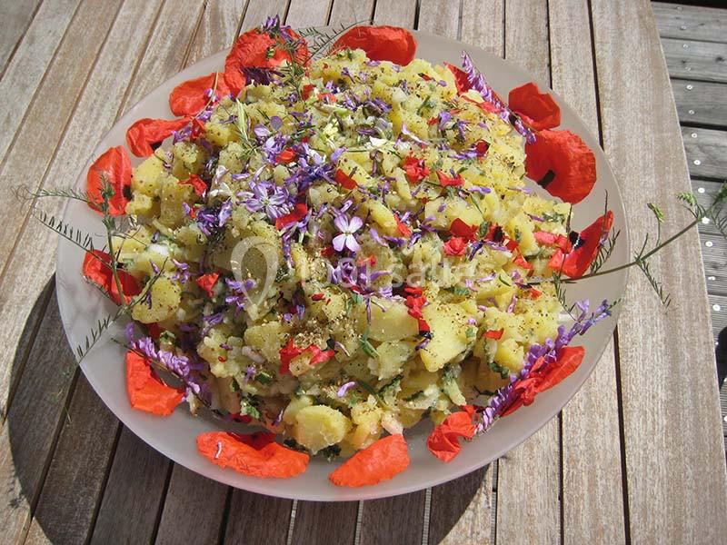 Salade de pommes de terre garnie de fleurs comestibles colorées, servie dans un plat sur une table en bois.