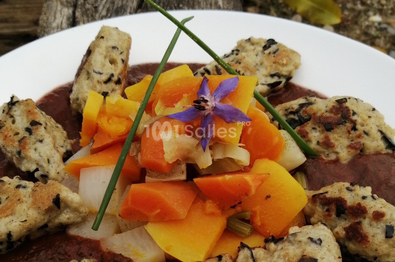 Assiette de légumes colorés avec quenelles grillées, garnie d'une fleur comestible et de brins de ciboulette.