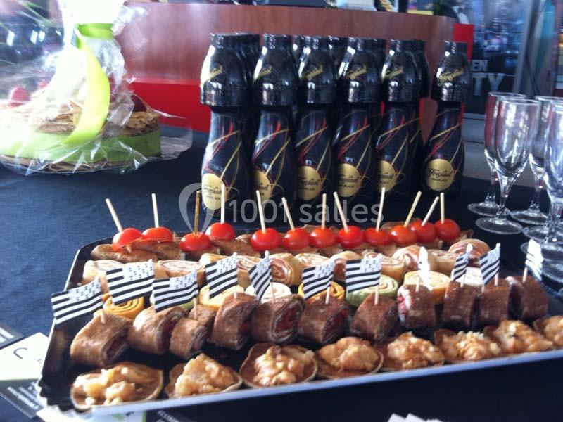 Plateau de bouchées apéritives variées avec des brochettes et des mini-feuilletés, accompagné de bouteilles et verres vides.