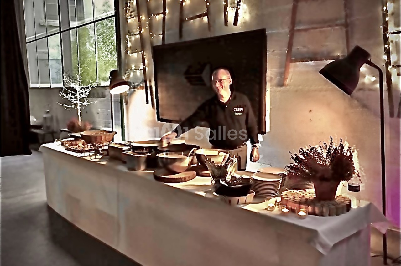 Un chef présente un buffet avec des plats variés, disposés sur une table éclairée dans un espace moderne et chaleureux.