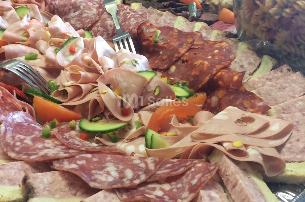 Plateau de charcuterie variée avec salami, mortadelle, chorizo et légumes frais en garniture.