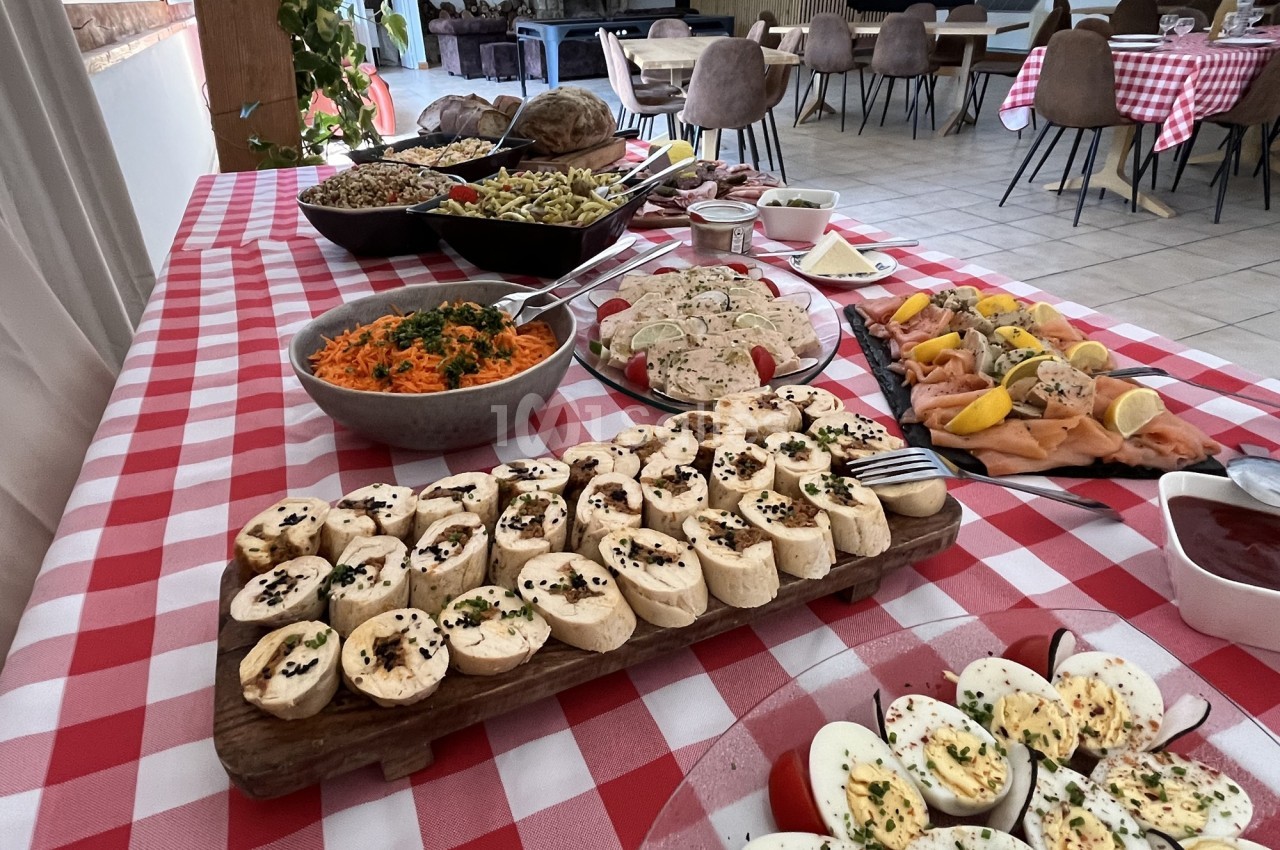 Buffet varié sur une table à nappe rouge et blanche, avec plats de légumes, charcuterie, saumon et fromages.