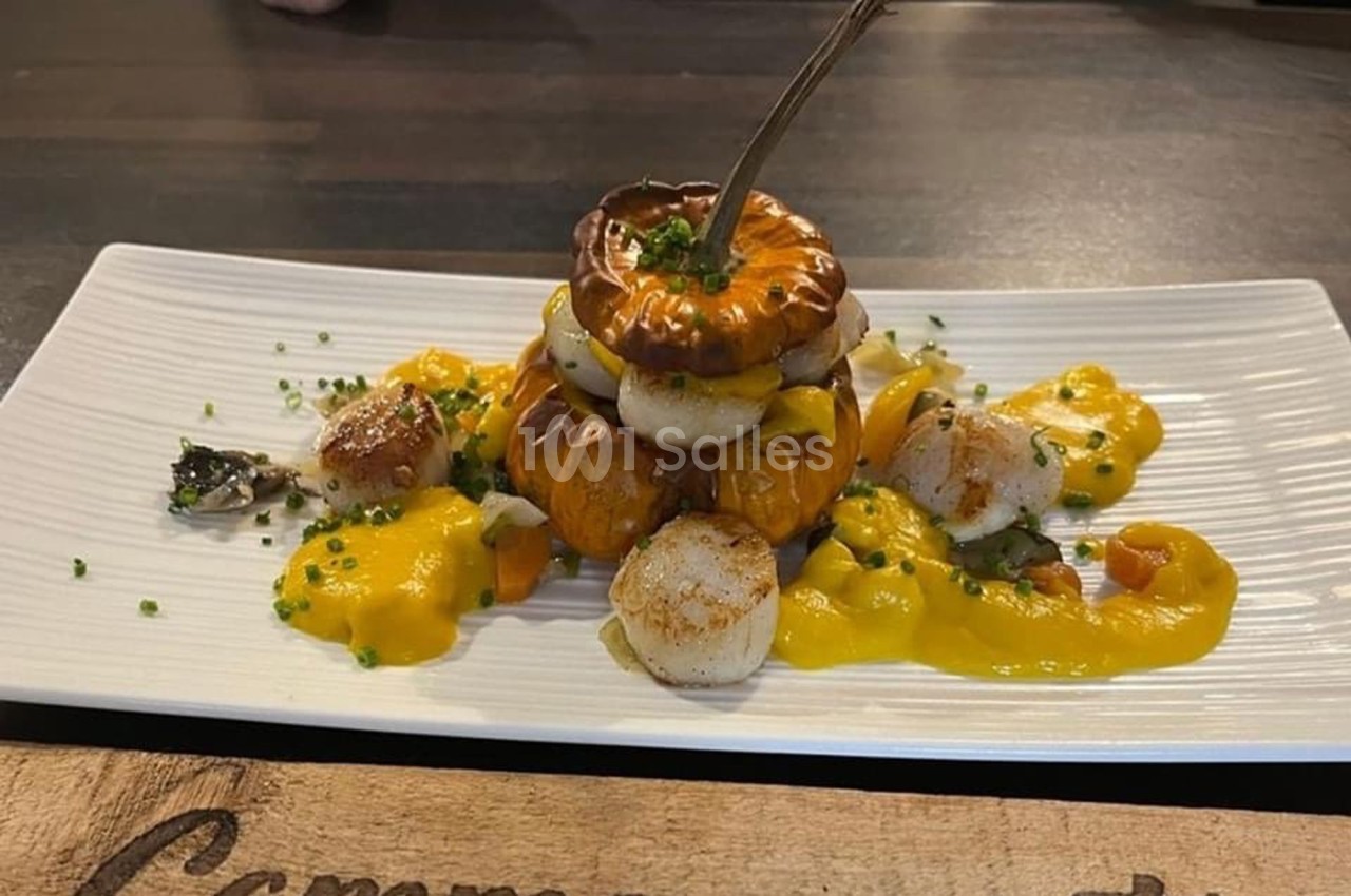 Assiette gastronomique composée de noix de Saint-Jacques, sauce jaune et légumes, présentée sur une assiette blanche.