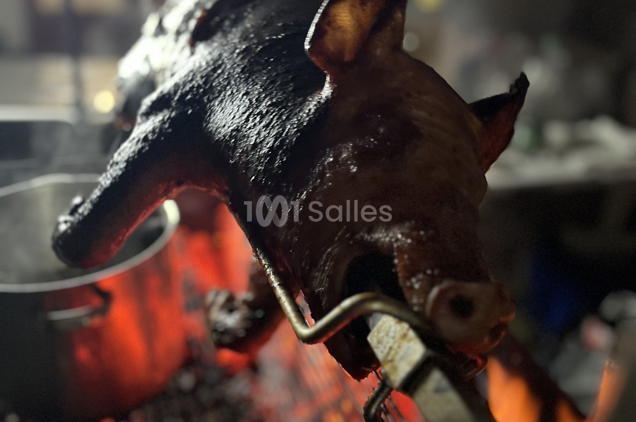 Cochon entier rôti à la broche au-dessus de braises rouges dans un environnement sombre.
