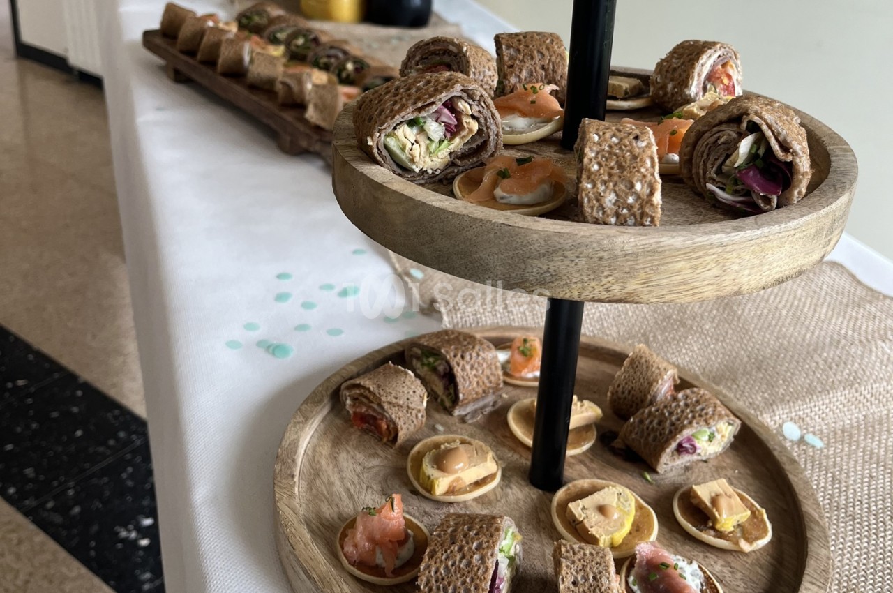 Plateaux en bois garnis de bouchées apéritives, notamment des roulés de galettes et des mini-tartelettes.