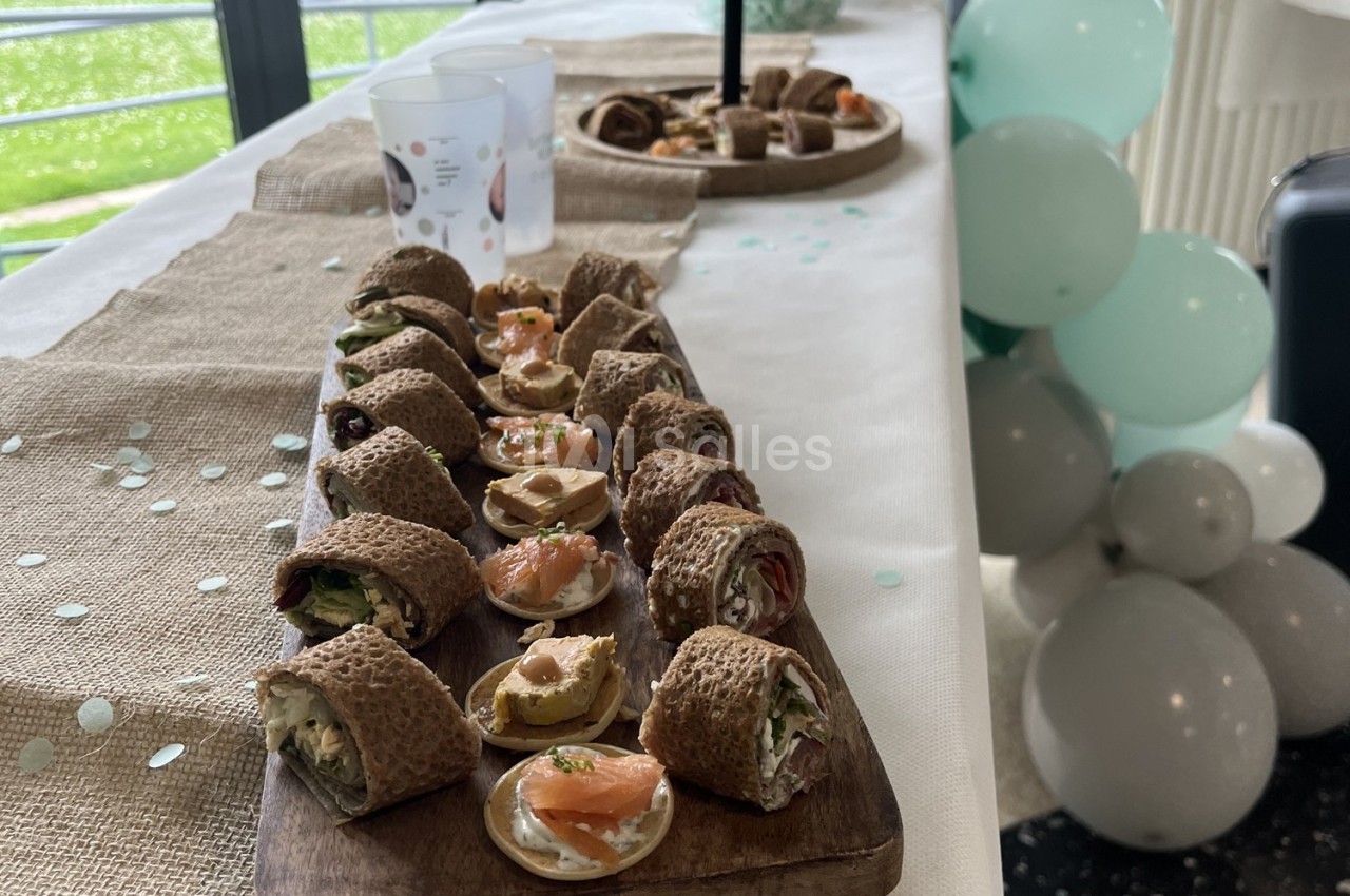 Plateau de bouchées apéritives variées sur une table décorée de ballons et de nappes en toile de jute.