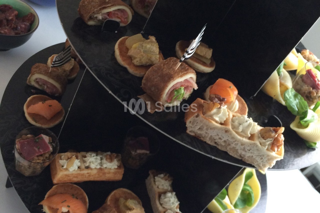 Plateau de service à étages présentant divers amuse-bouches salés, dont des verrines, toasts et roulés.