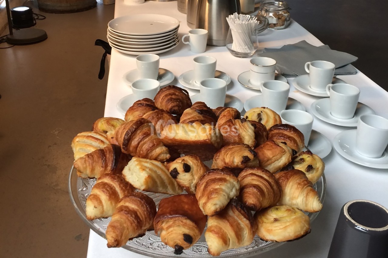 Plateau de viennoiseries variées sur une table dressée avec des tasses, des assiettes et des accessoires pour le café.