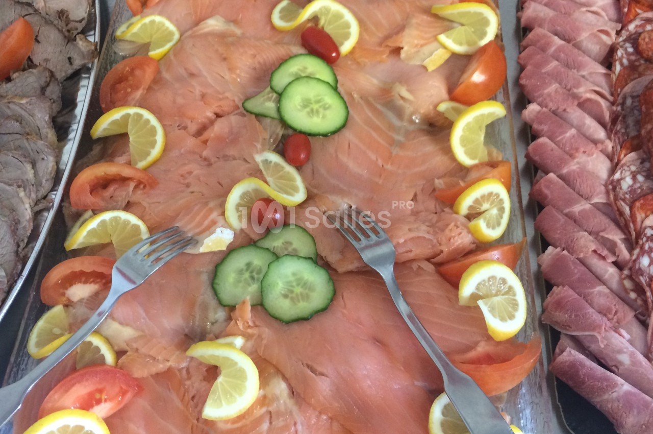 Plateau de saumon fumé garni de tranches de citron, tomates, concombres et tomates cerises, avec deux fourchettes.