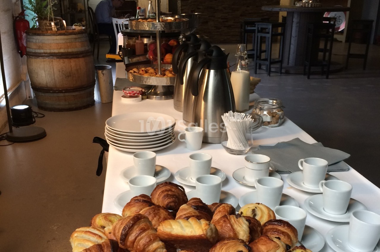 Table dressée avec viennoiseries, tasses, assiettes, cafetières et accessoires, dans un espace intérieur convivial.