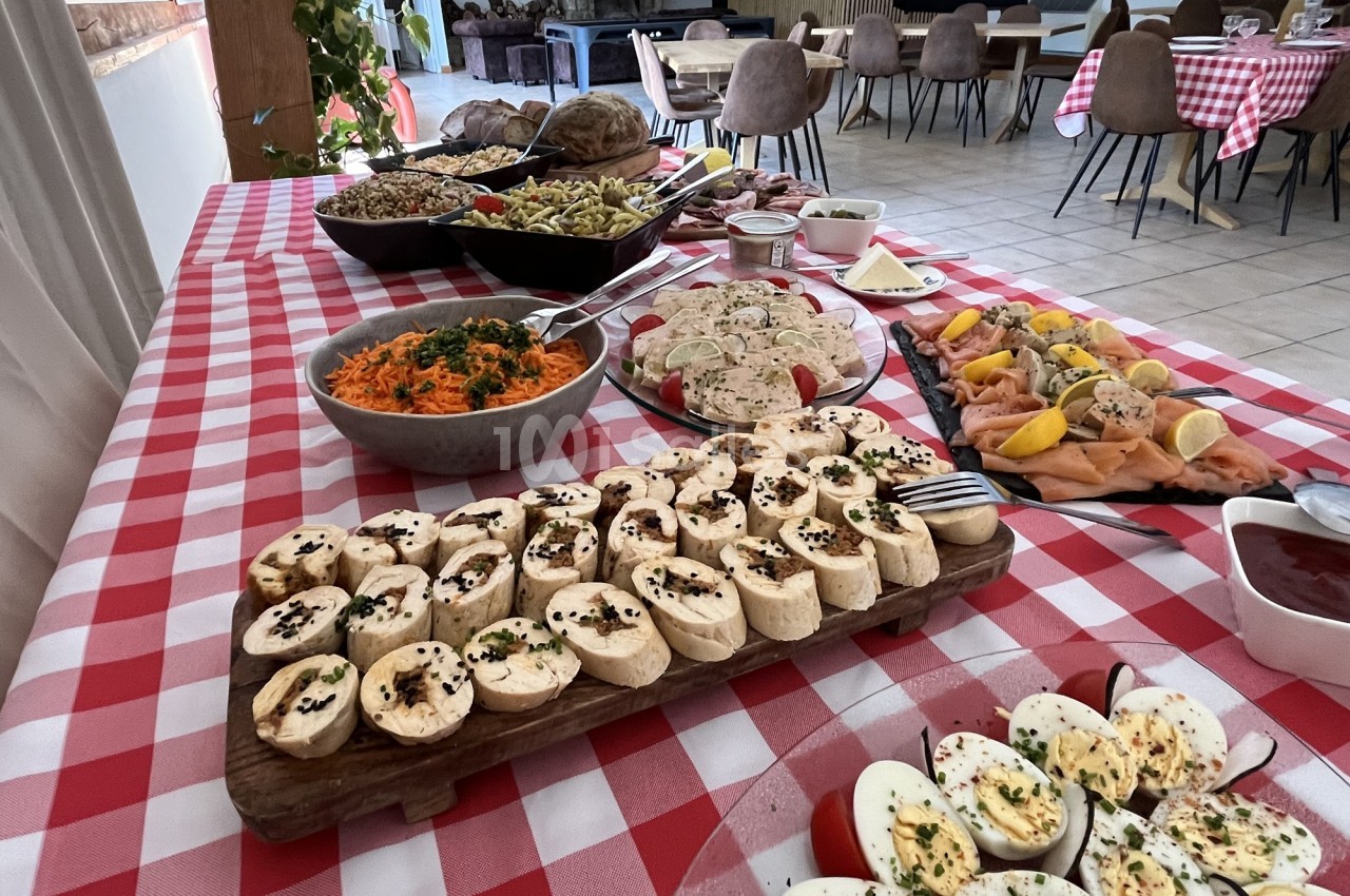 Buffet varié sur une table à nappe rouge et blanche, avec plats de légumes, charcuterie, saumon et fromages.