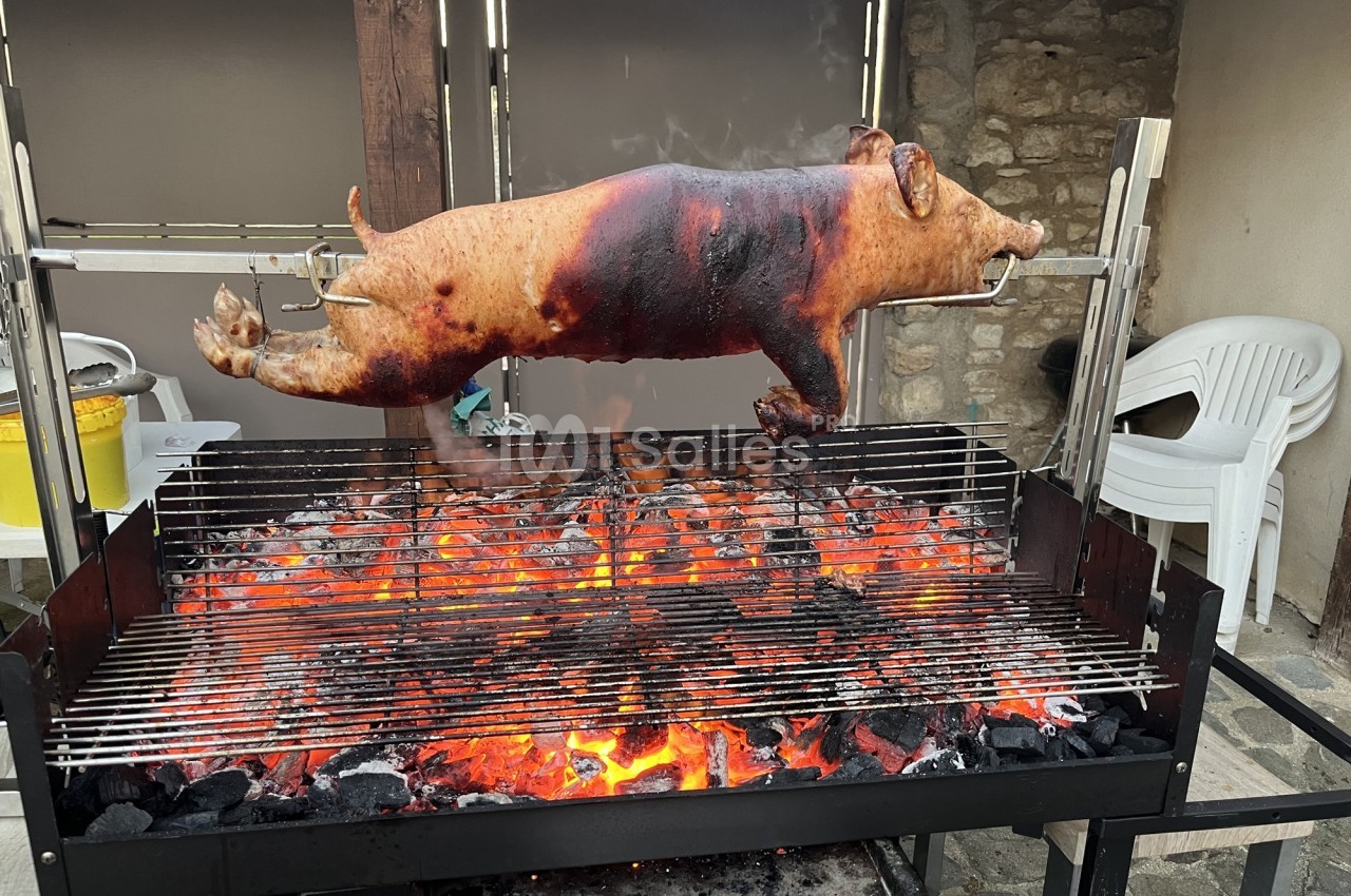 Cochon entier rôti à la broche au-dessus d'un barbecue à charbon avec flammes et braises rouges.