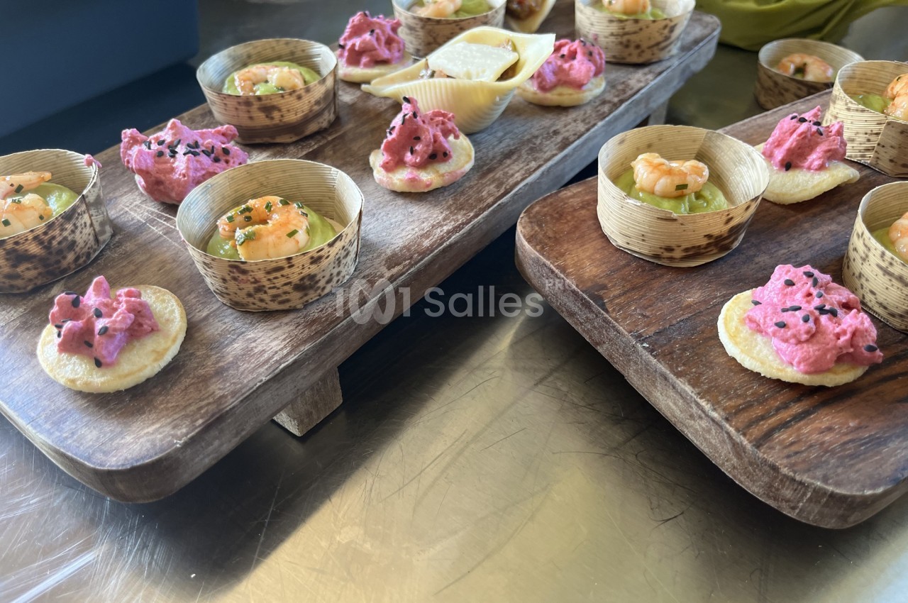 Plateaux en bois garnis de bouchées apéritives colorées, dont des tartinades roses et des crevettes sur des bases…