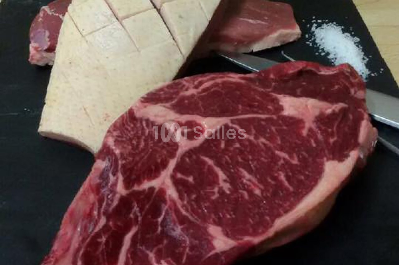 Tranche de viande rouge marbrée, magret de canard incisé et sel sur une planche noire avec un couteau.
