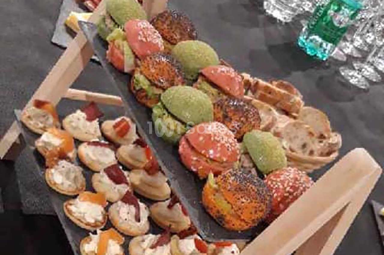 Plateau de mini-burgers colorés et assortiments de canapés sur une table dressée pour un buffet.
