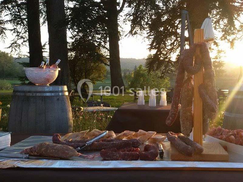 Plateau de charcuterie disposé sur une table en extérieur, avec un paysage boisé et un coucher de soleil en arrière-plan.