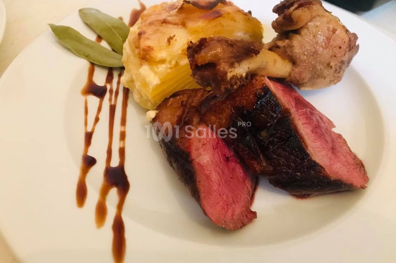Assiette composée de viande grillée, gratin de pommes de terre, sauce balsamique et feuilles de laurier en décoration.