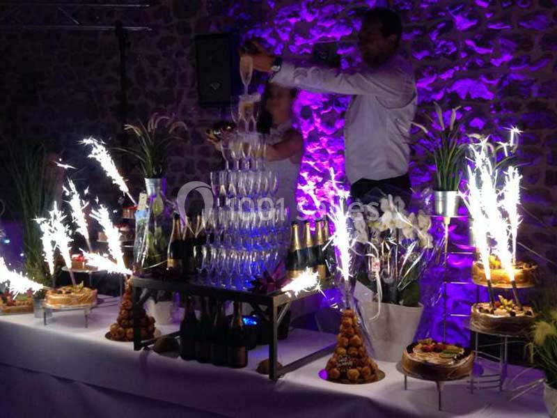 Tour de coupes de champagne illuminée par des étincelles, entourée de gâteaux et de décorations florales.